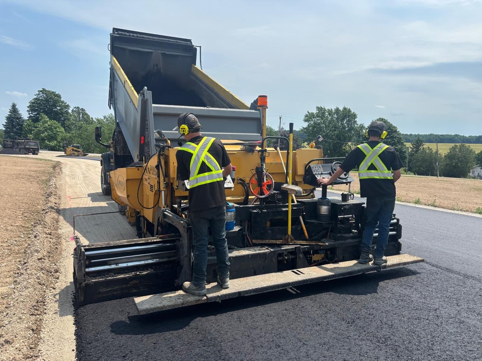 A paving crew reviewing customer feedback on a tablet outside their truck at a residential job site, with a freshly paved driveway in the background