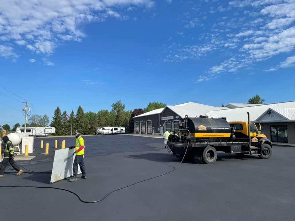 A pavement contractor and office manager reviewing customer feedback together on a tablet beside their work truck at a freshly sealed parking lot